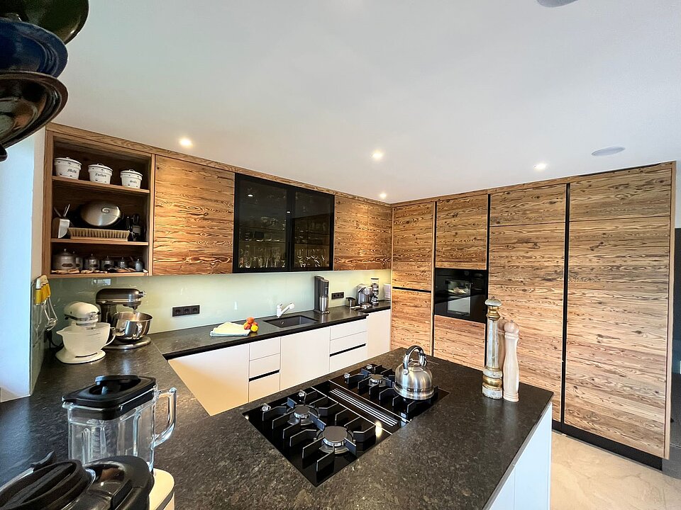 Küche mit Kochinsel mit schwarzer Steinarbeitsplatte und Hochschränken in Altholz