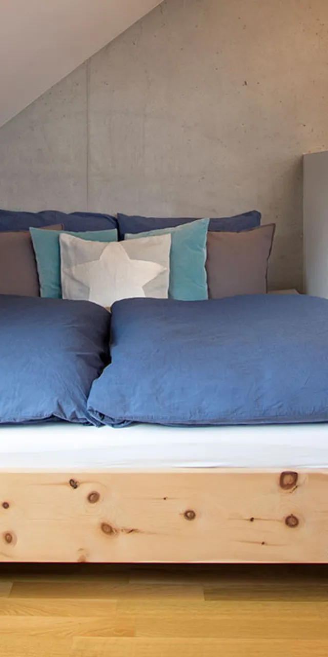 Modernes Schlafzimmer im Dachgeschoss mit Holzbett, blauer Bettwäsche und weißem Sofa