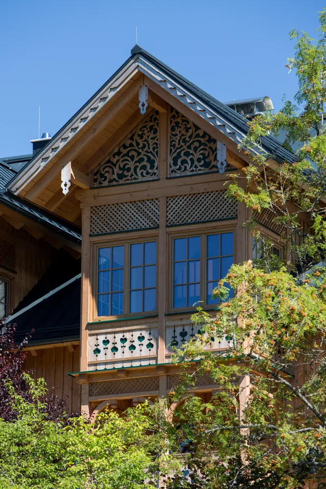 Detail eines traditionellen Holzhauses mit geschnitztem Giebel und blauen Fenstern an einem sonnigen Tag