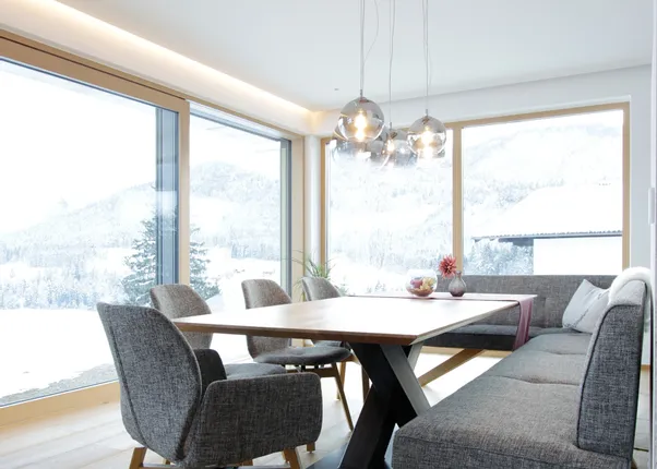 Modernes Esszimmer mit Holzfußboden, grauen Polstermöbeln und Panoramablick auf verschneite Berge