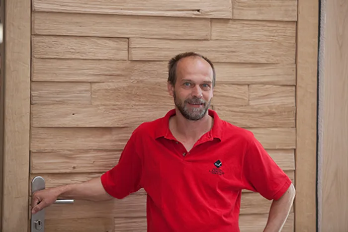 Mann mit rotem Poloshirt lehnt locker an einer Holztür