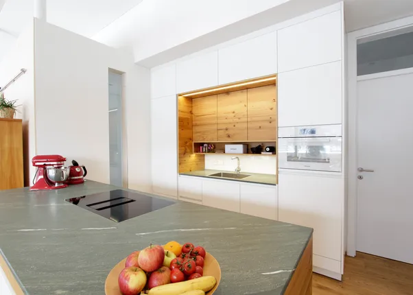 Moderne Küche mit weißem Design, Holzrückwand, Kochinsel und frischem Obst auf der Arbeitsplatte