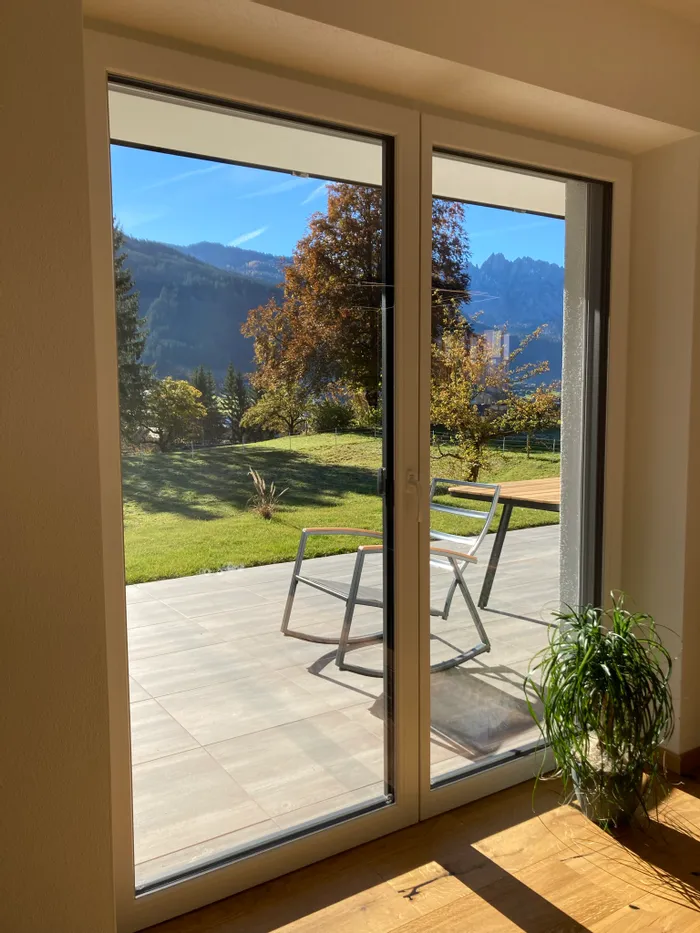 Terrasse mit Stuhl und Bergblick durch großes Fenster an einem sonnigen Tag