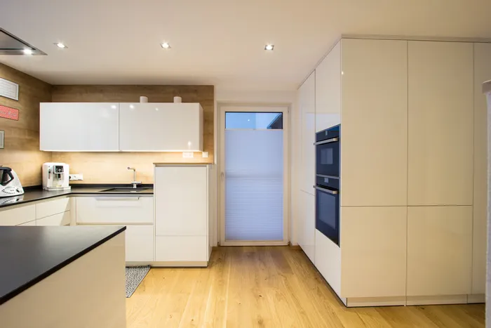 Moderne Einbauküche mit weißen Hochglanzfronten, Holzfußboden und integrierten Geräten