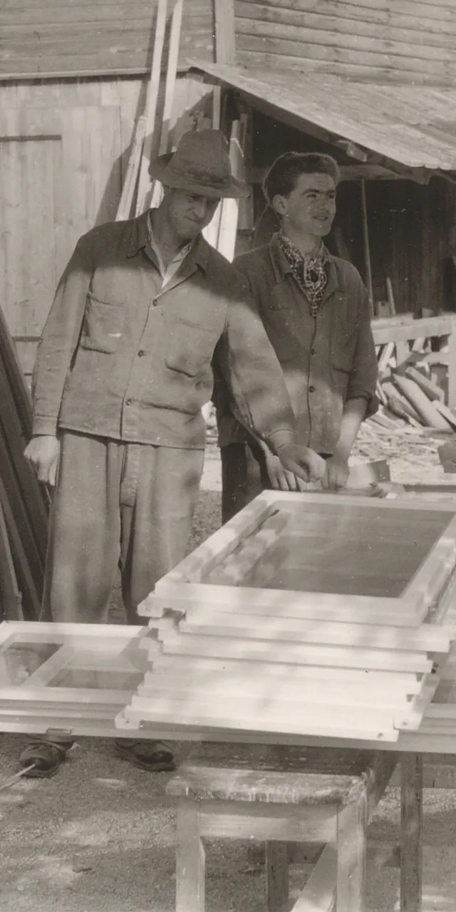 Vier Schreiner arbeiten im Freien an Holzrahmen vor einer Werkstatt