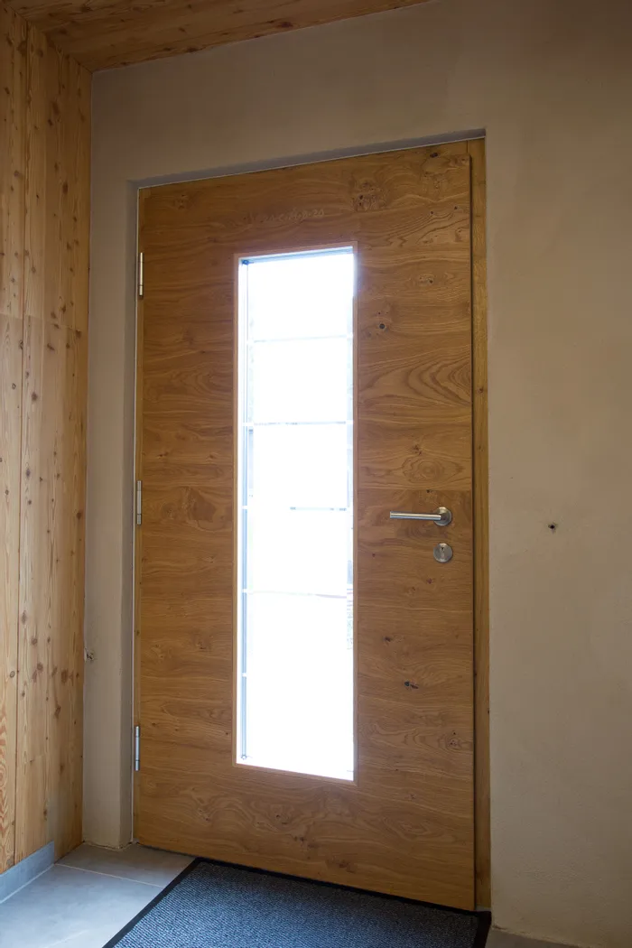 Massivholztür mit schmalem Glaseinsatz und Edelstahlgriff im modernen Eingangsbereich