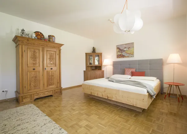 Helles Schlafzimmer mit Holzboden, Doppelbett, geschnitztem Kleiderschrank und moderner Beleuchtung