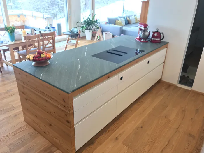 Moderne Kücheninsel mit grünem Naturstein, Obstschale und roten Küchengeräten auf Holzfußboden