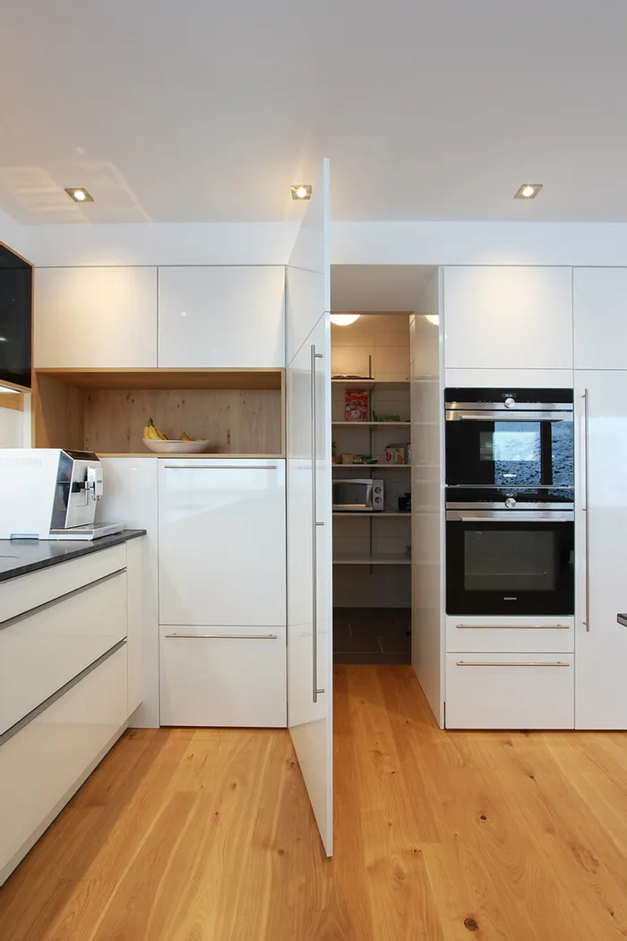 Versteckte Speisekammer in einer weißen Küche mit viel Stauraum für Vorräte