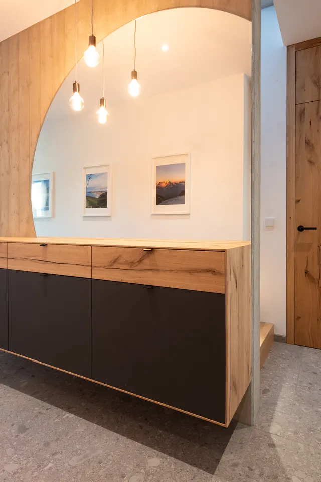 Moderner Flur mit Holz-Kommode, großem Spiegel, Designerlampen und Holztür auf Steinboden