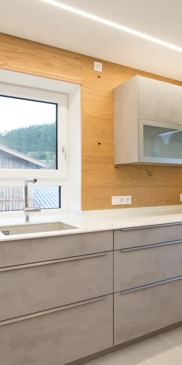 Moderne Küche mit grauen Schränken, Holzverkleidung und großen Fenstern mit Ausblick