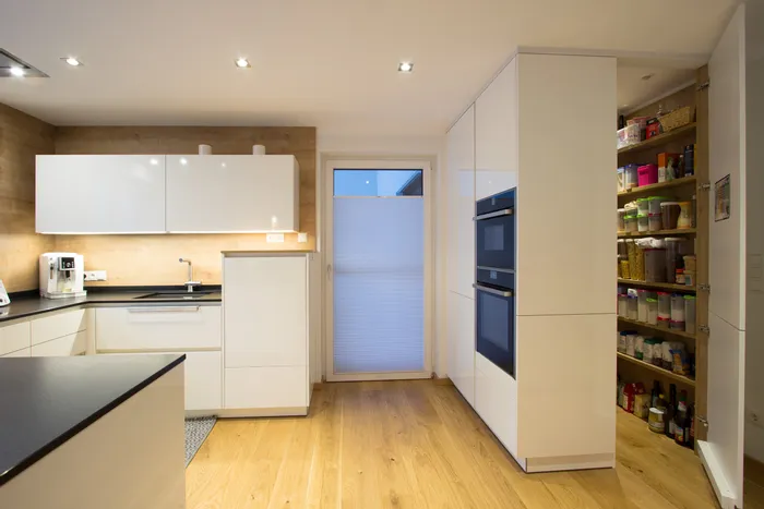 Moderne weiße Küche mit Holzfußboden und offenem Vorratsschrank mit Lebensmitteln
