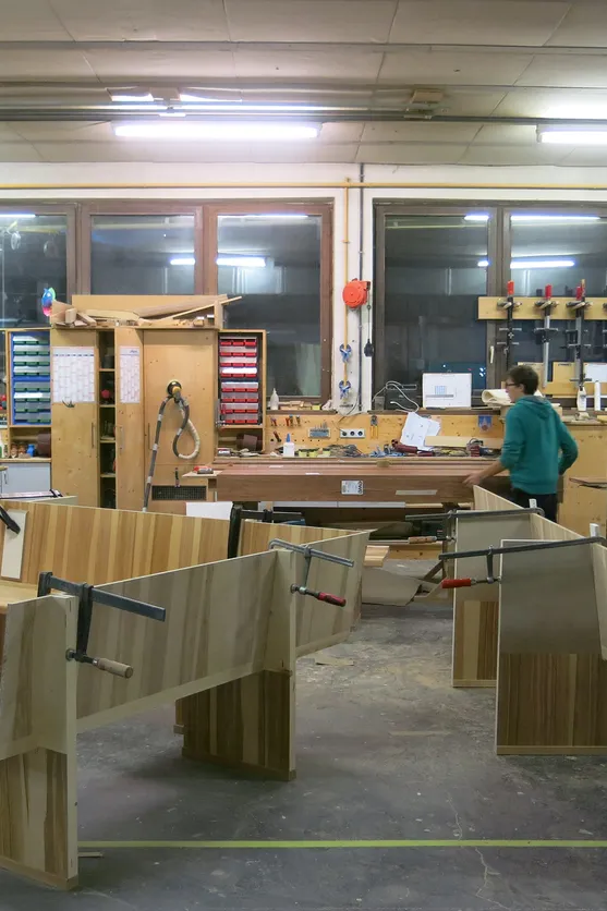 Holzwerkstatt mit Werkbänken, Holzverkleidungen und arbeitender Person bei der Möbelherstellung