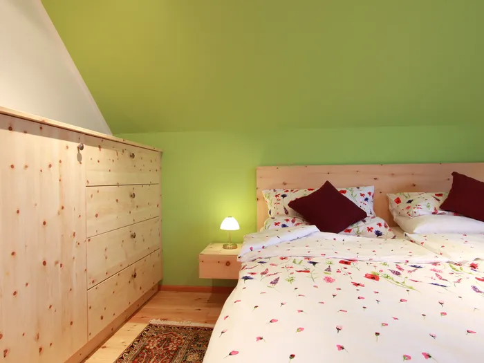 Gemütliches Schlafzimmer mit Holzbettrahmen, grüner Wandfarbe und floraler Bettwäsche