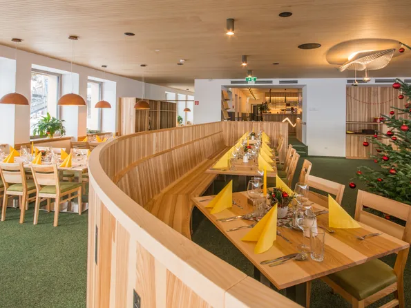 Modernes Restaurant mit Holzmöbeln, festlich gedeckten Tischen und Weihnachtsbaum mit roten Kugeln