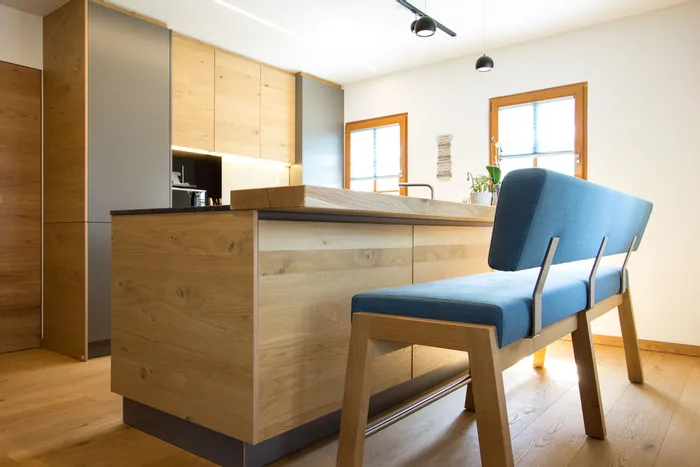 Moderne Wohnküche mit Kücheninsel aus Holz und blauer Polsterbank im natürlichen Licht