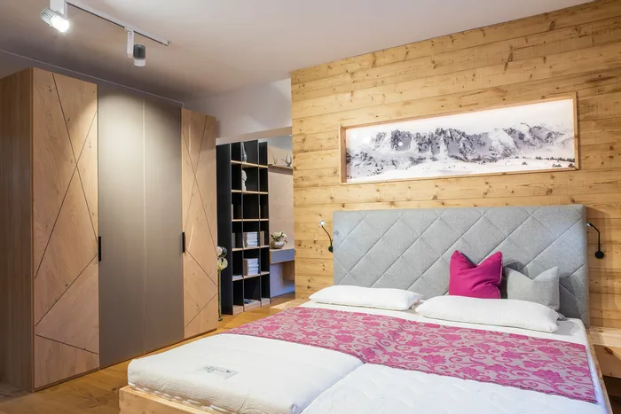 Modernes Schlafzimmer mit Holzwand, grauem Polsterbett und pinker Tagesdecke