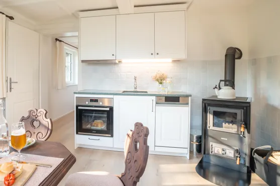 Helle Landhausküche mit weißem Ofen, Holzofen, Esstisch und frischem Brot im Backofen