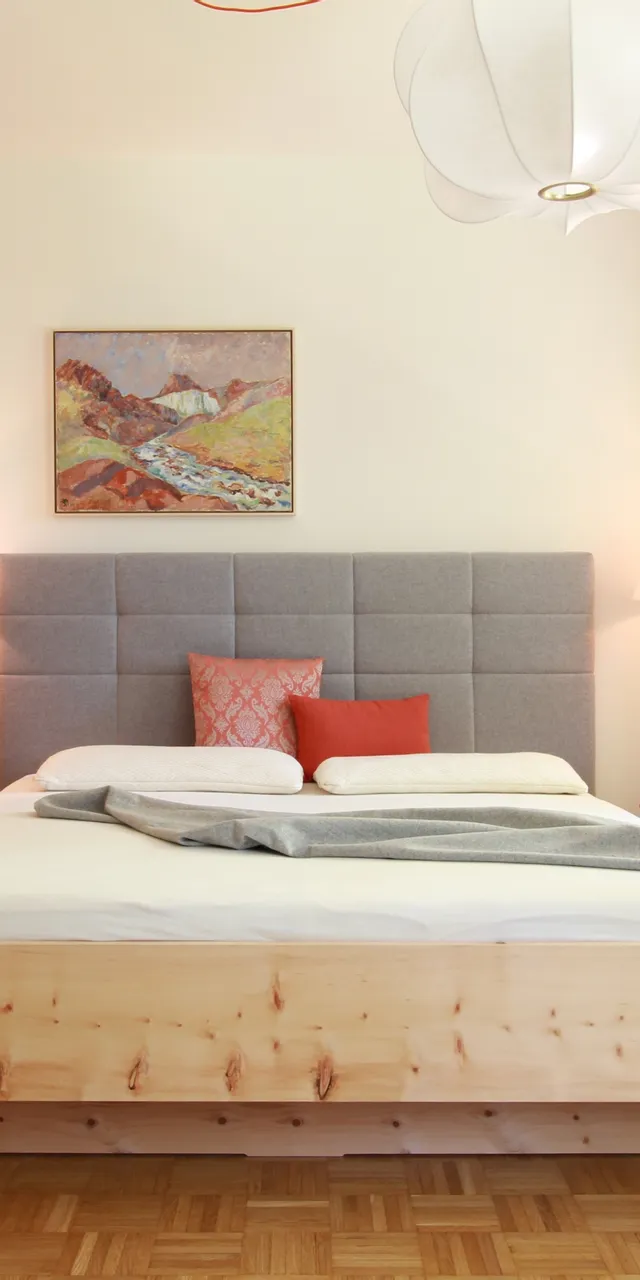 Modernes Schlafzimmer mit grauem Polsterbett, Holzmöbeln und dezenter Beleuchtung