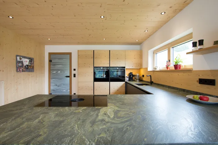 Moderne Küche mit hellem Holz, schwarzen Geräten und grün-grauer Naturstein-Arbeitsplatte