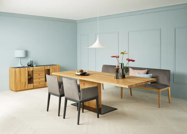Moderne Esszimmereinrichtung mit Holztisch, grauer Sitzbank und hellblauer Wand