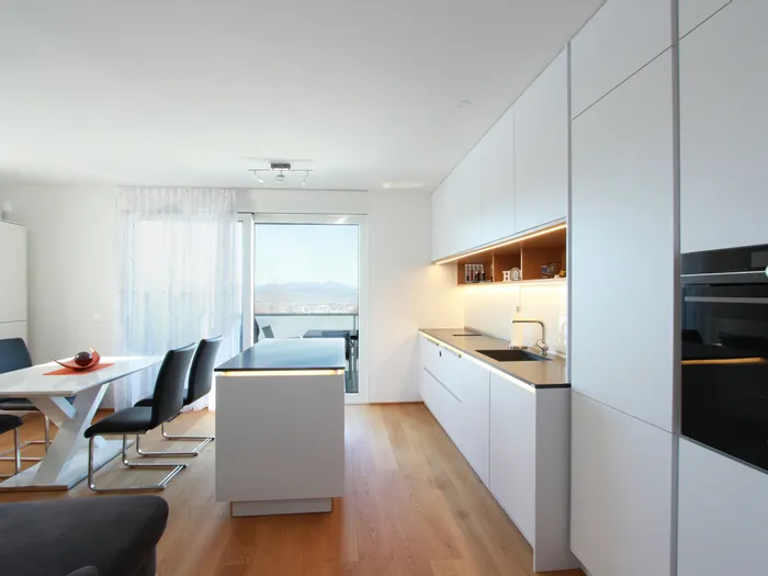 Moderne weiße Einbauküche mit Kochinsel und Essbereich mit Aussicht auf Balkon