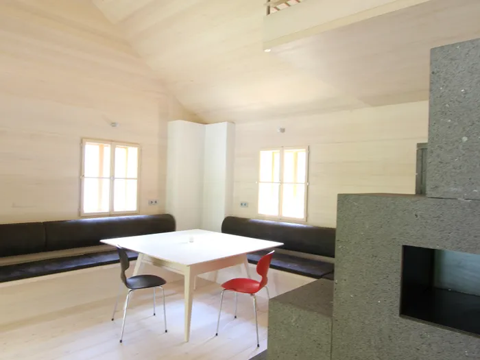 Modernes Wohnzimmer mit Holzwänden, Essbereich, schwarzen Bänken und Ofen mit grauer Steinverkleidung