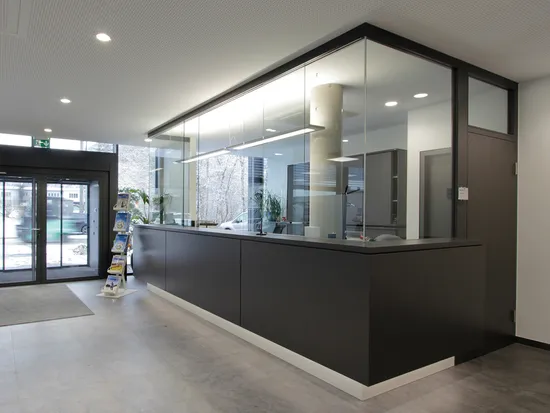 Moderne Empfangshalle mit schwarzem Tresen, Glaswänden und Prospektständern bei Tageslicht