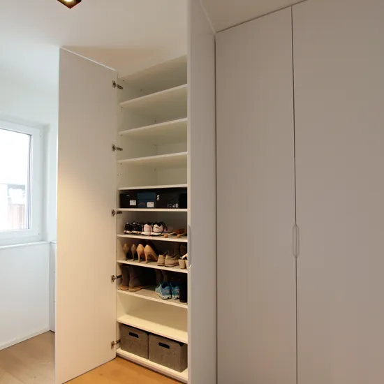 Geöffneter weißer Einbauschrank mit Regalen für Schuhe und Aufbewahrungsboxen