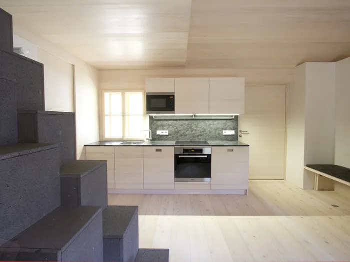 Moderne minimalistische Küche mit hellen Holzmöbeln und schwarzer Treppe im offenen Wohnbereich