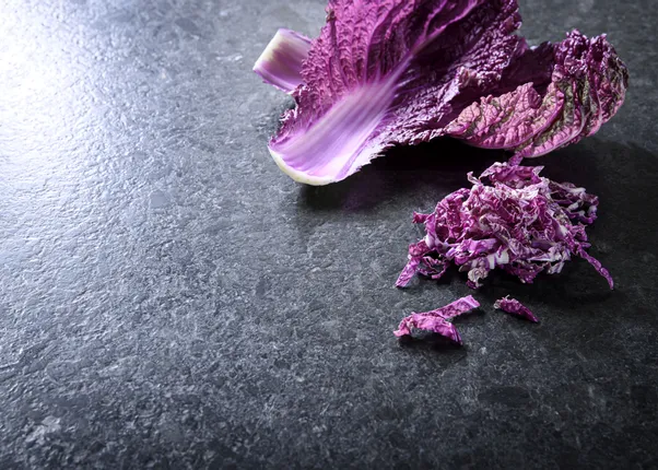 Lila Chinakohl und fein geschnittener Kohlstreifen auf dunkler Steinoberfläche