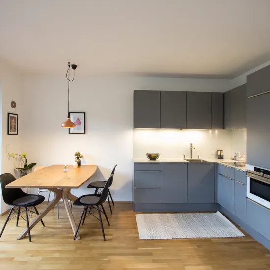 Moderne Einbauküche mit grauen Schränken, Holz-Esstisch und Stühlen auf Parkettboden