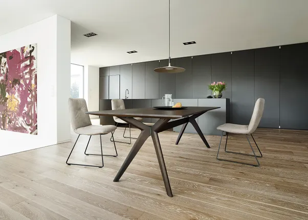 Moderne Küche mit dunklen Schränken, Holztisch, beigen Stühlen und abstrakter Wandkunst