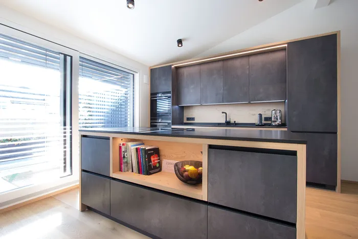 Moderne Küche mit dunklen Schränken, Kochinsel, eingebauten Büchern und Obstschale