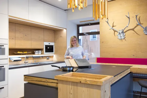 Moderne Holzküche mit Kochinsel, stilvollen Hängelampen und Frau mit Musterplatten