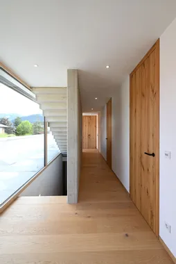 Moderner Innenflur mit Holzfußboden, Holztüren und großem Fenster mit Blick ins Grüne