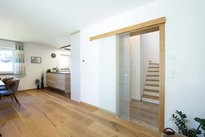 Helles modernes Wohnzimmer mit Holzboden, Glastür und Treppe im Hintergrund