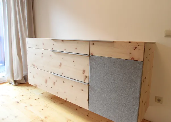 Moderne Hängeschrankkommode aus hellem Holz mit grauer Stofftür in minimalistischem Raum