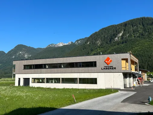 Modernes Gebäude der Tischlerei Laserer vor Alpenkulisse an sonnigem Tag