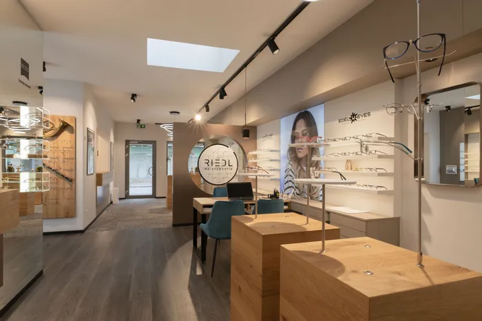 Modernes Optikergeschäft mit Brillenausstellung, Beratungstischen und Werbeposter von Edel-Eyes