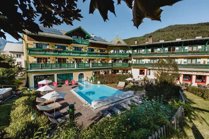 Traditionelles Hotel mit Balkon und Außenpool in Alpenlage bei sonnigem Wetter