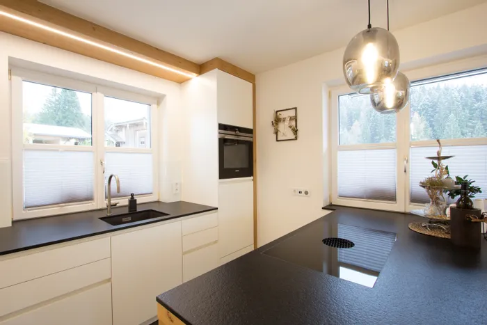 Moderne Küche mit weißen Schränken, schwarzer Arbeitsplatte und großem Fensterblick