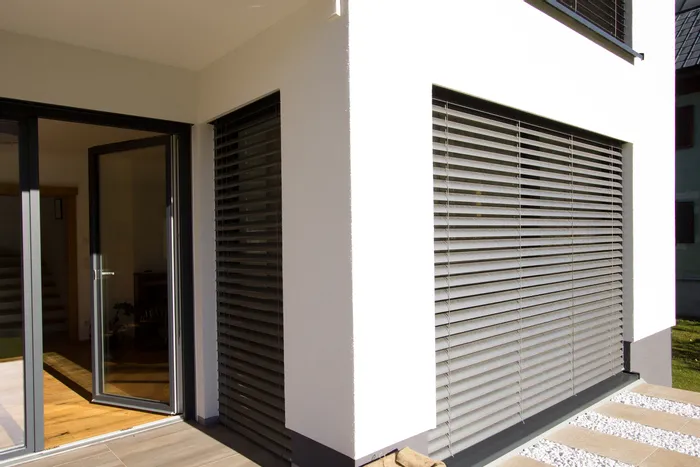 Moderne Fassade mit großen Fenstern und geschlossenen Außenjalousien im Sonnenschein