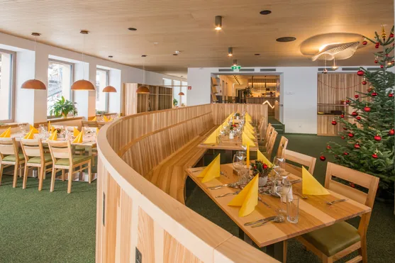 Modernes Restaurant mit Holzmöbeln, festlich gedeckten Tischen und Weihnachtsbaum mit roten Kugeln