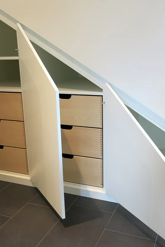 Maßgeschneiderter Einbauschrank unter Dachschräge mit offenen weißen Türen und Holzschubladen