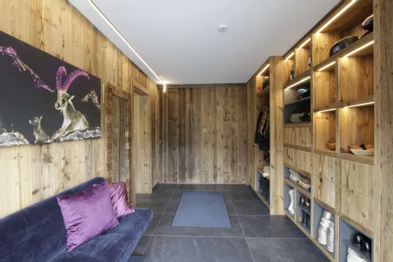 Moderner Garderobenbereich mit Holzverkleidung, offenen Regalen und dunkelblauem Sofa mit lila Kissen