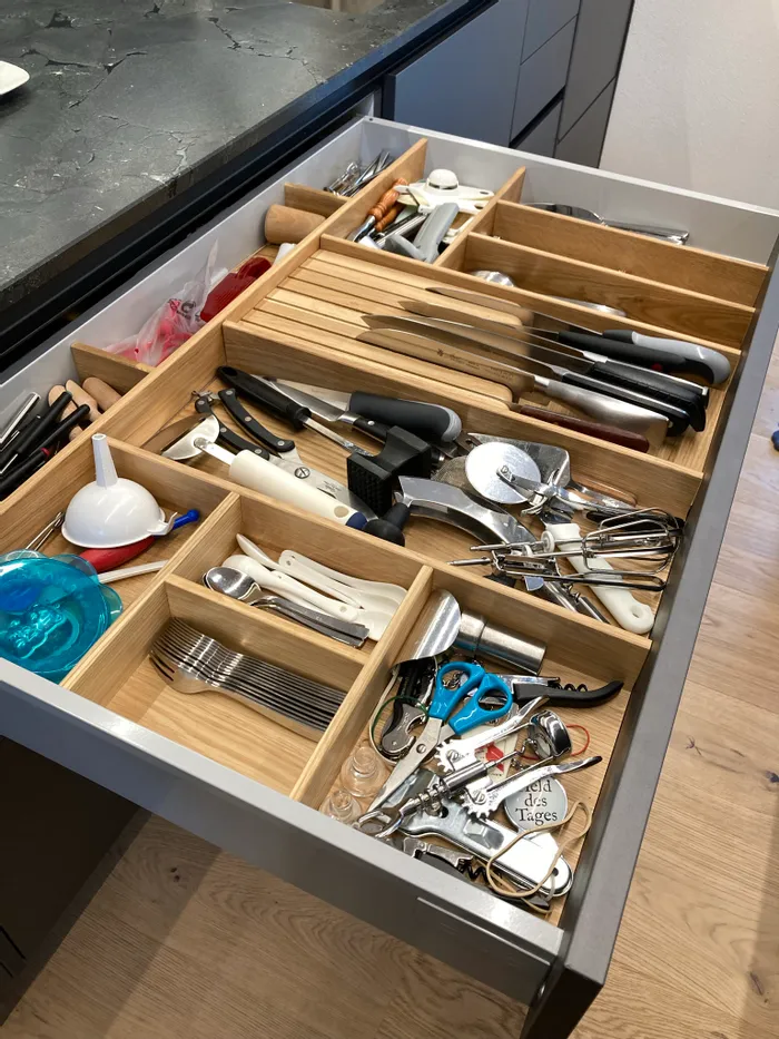 Offene Küchenschublade mit ordentlich sortierten Messern und Küchenutensilien im Holz-Einsatz