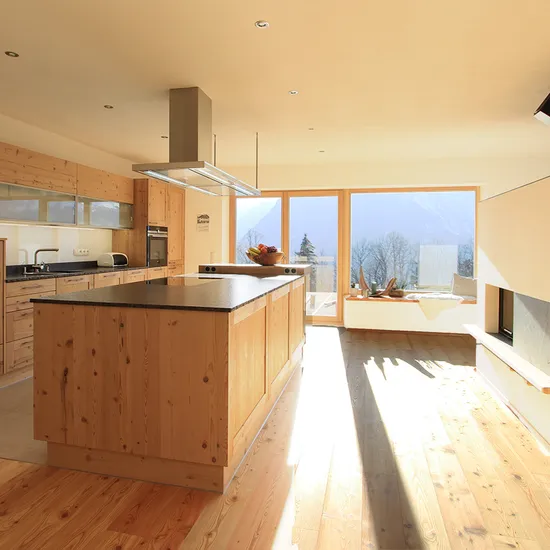 Helle moderne Wohnküche mit Holzverkleidung, Kochinsel und Panoramafenster mit Bergblick