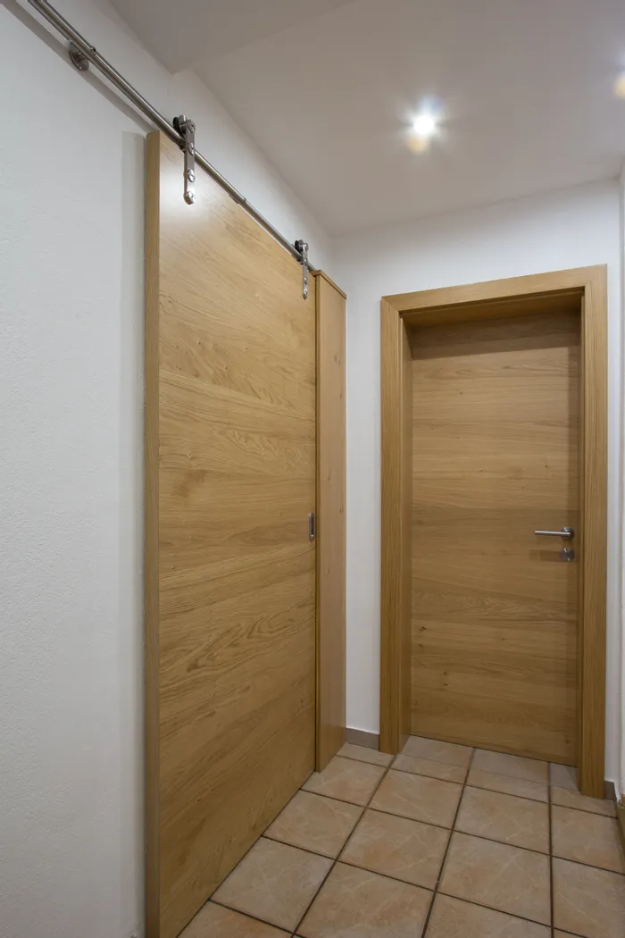 Flur mit Holzdrehtür und Schiebetür aus hellem Holz auf gefliestem Boden