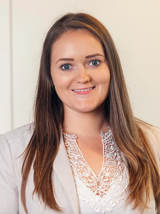 Junge Geschäftsfrau mit langen braunen Haaren und beigem Blazer lächelt in einem Büro